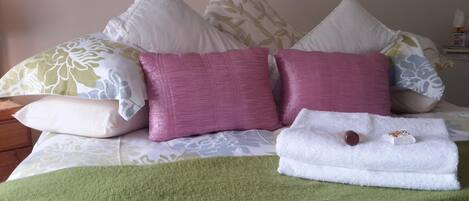 A bed with multiple pillows, a green throw blanket, and a folded white towel with a brown object on it.