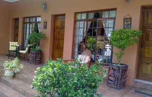 A covered outdoor seating area with chairs and tables, potted plants, and a wooden door.