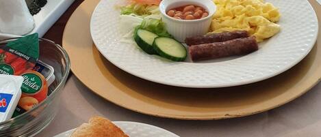 A breakfast setting with toast, scrambled eggs, bacon, tomatoes, cucumbers, and beans on a plate, along with a cup of coffee and a glass of water.