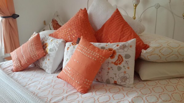 Una cama con varias almohadas, cabecera blanca y edredón estampado.