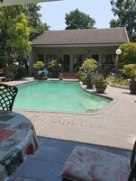 A pool area with a tiled deck, a table with a tablecloth, and potted plants.