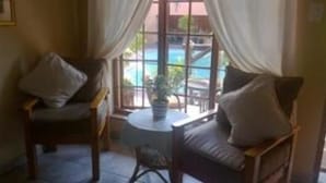 Une pièce avec deux chaises en bois et une petite table ronde, une fenêtre avec des rideaux et une vue sur une piscine.