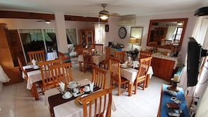 Un coin repas avec des tables et des chaises en bois, une horloge au mur et un téléviseur sur le côté droit.