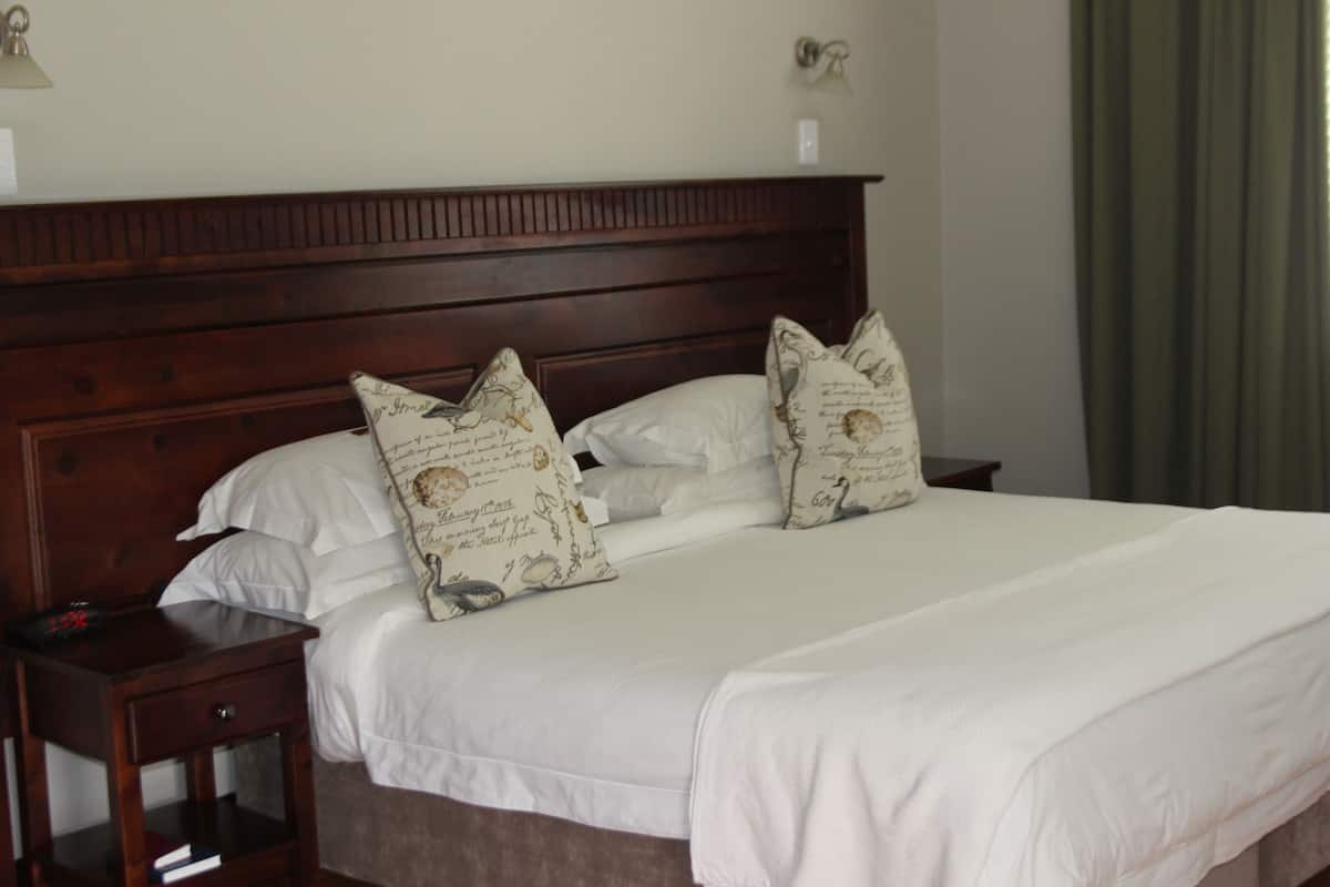 A neatly made bed with white linens and decorative pillows, a wooden headboard, and a bedside table with a lamp.