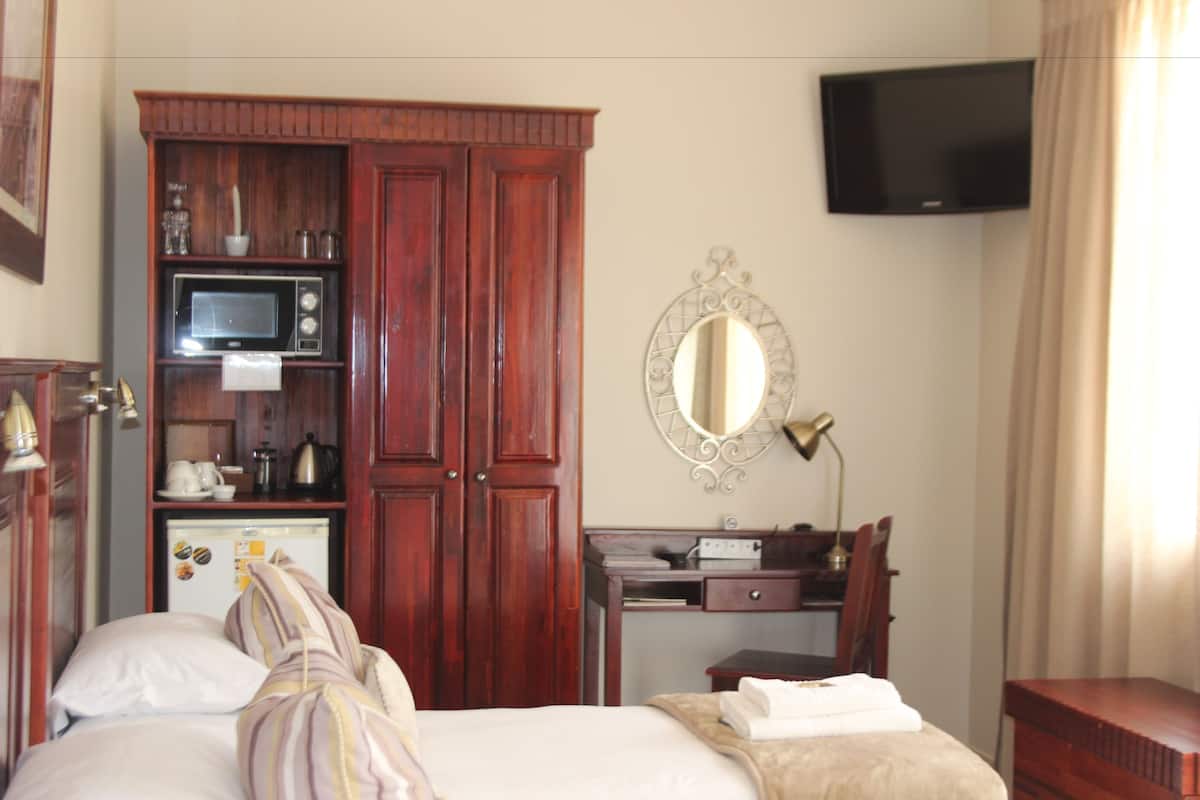 A hotel room with a bed, a wardrobe, a desk with a mirror, a television, and a small refrigerator.