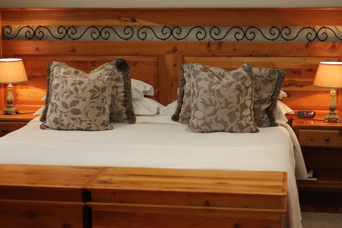 A neatly made bed with floral-patterned pillows, wooden headboard, and bedside lamps.