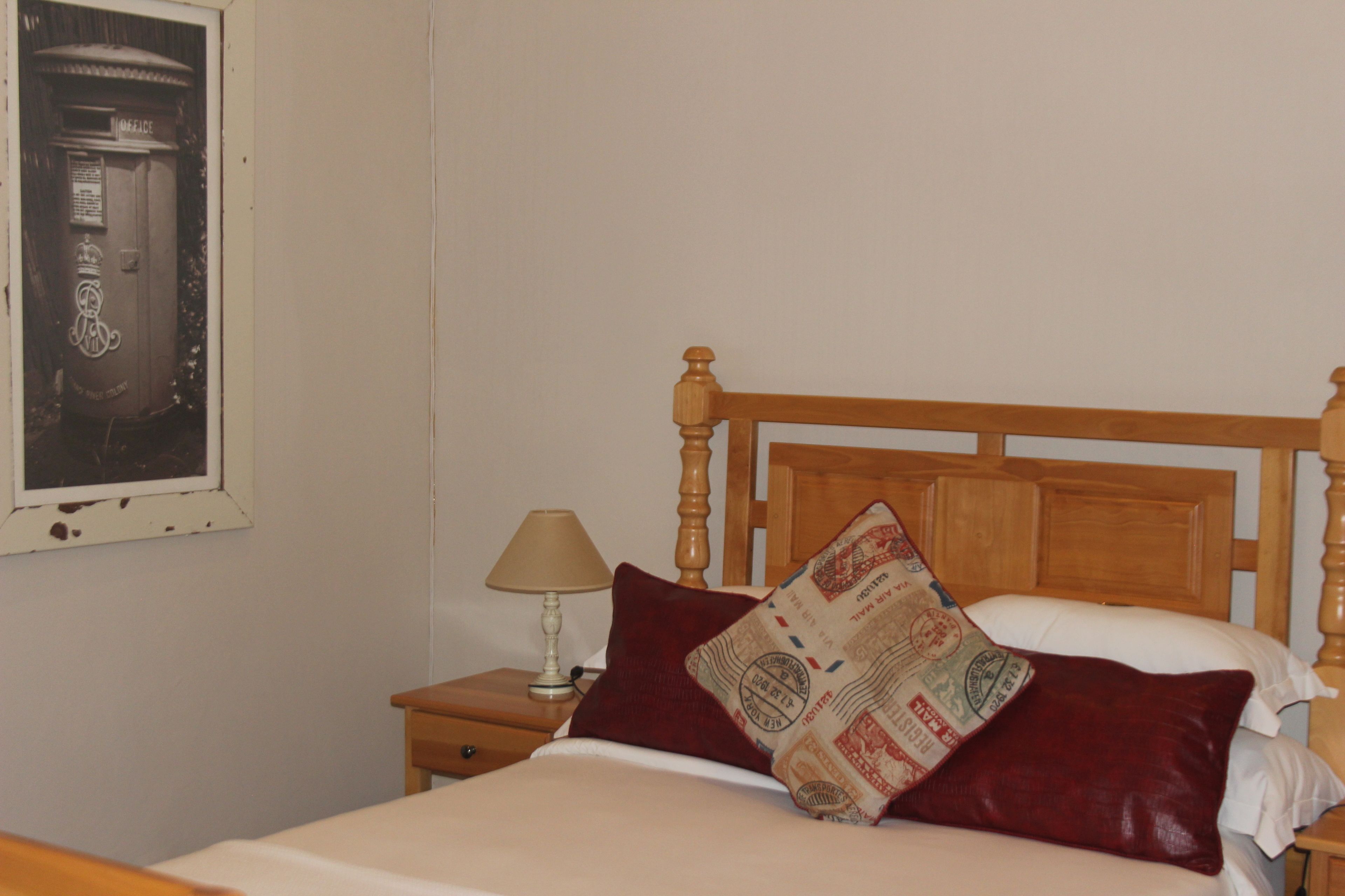 Una cama con cabecera de madera, una mesita de noche con lámpara y un buzón fijado a la pared.