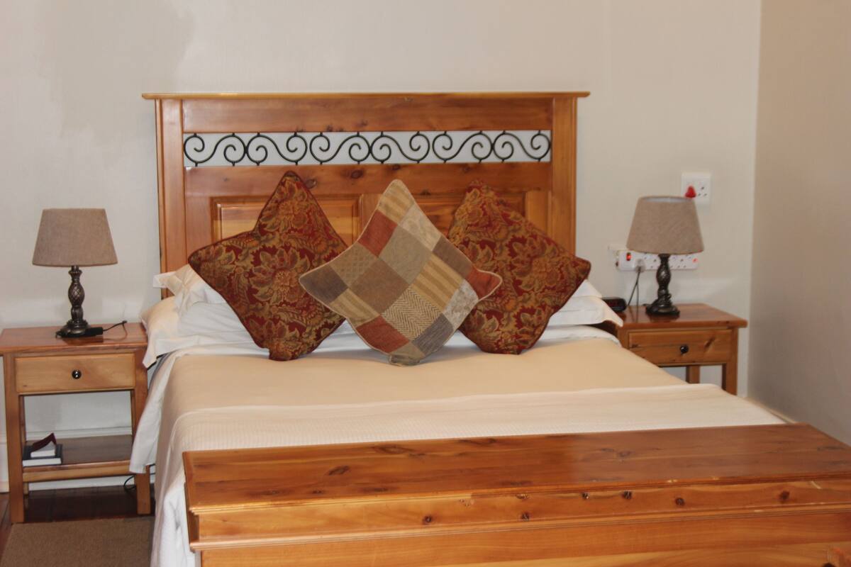 A neatly made bed with a wooden headboard, two bedside tables with lamps, and decorative pillows.