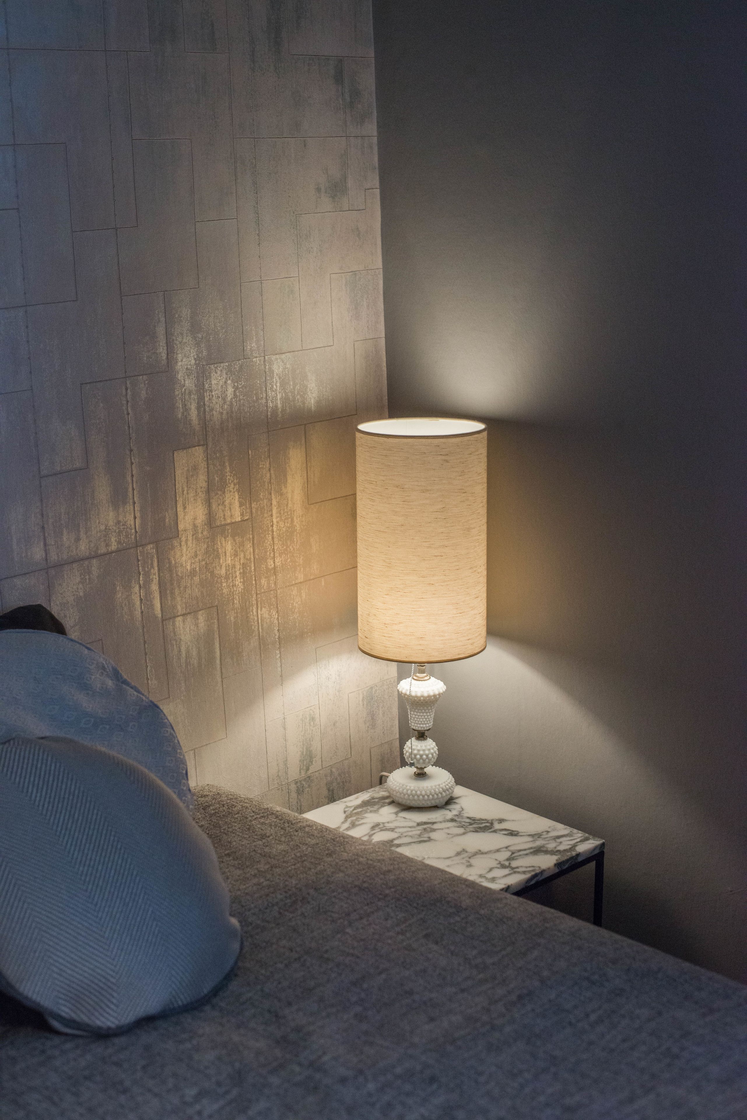 Una habitación moderna con una mesita de noche de diseño marmolizado, una lámpara y una pared con textura.