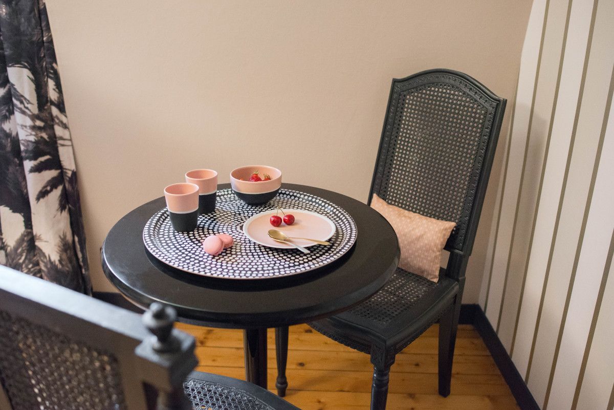 Una pequeña mesa redonda con un mantel individual blanco y negro, dos tazas rosas, un cuenco con fresas y un plato con una cuchara.