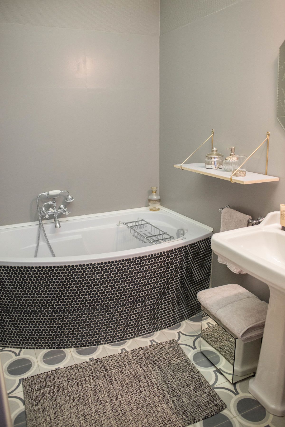 Une salle de bain moderne avec une baignoire sur pieds, un lavabo blanc et une petite étagère contenant des articles de toilette.