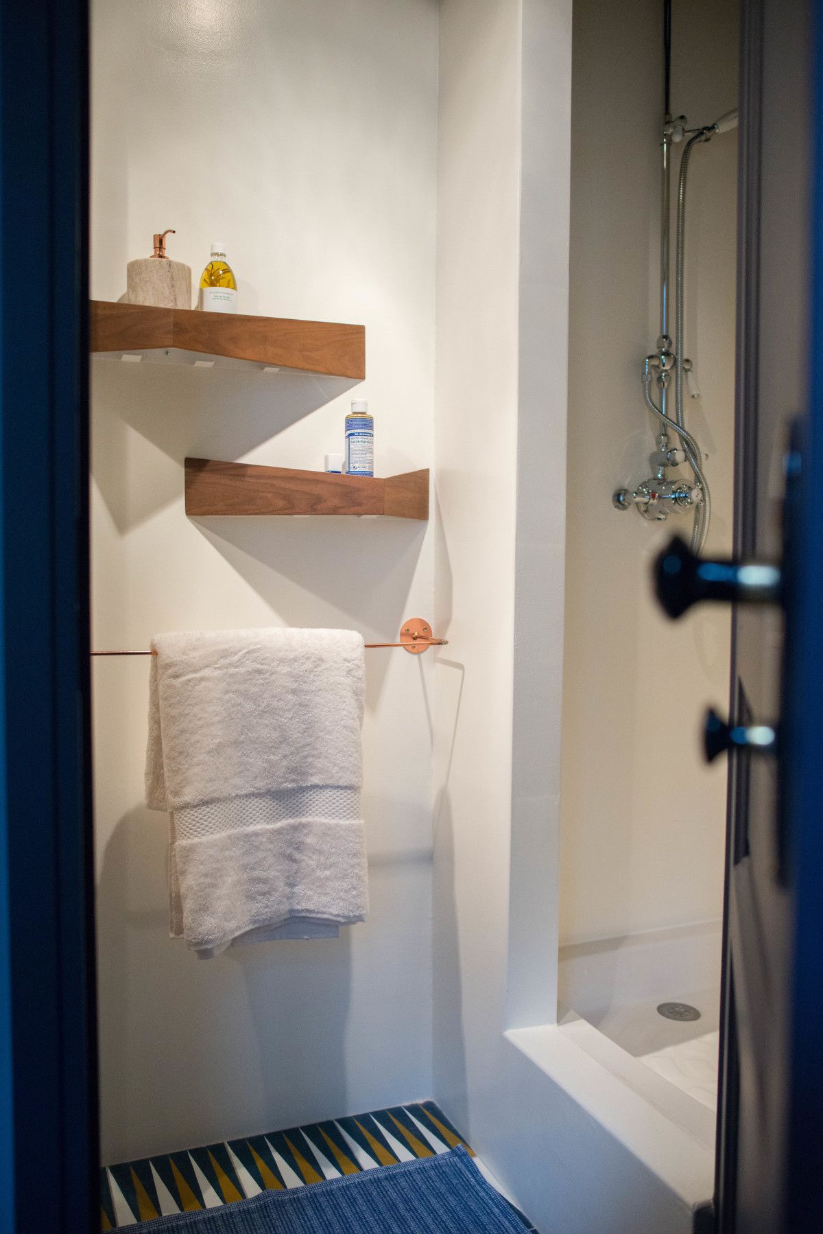 Un baño con ducha, un perchero y dos estantes de madera con artículos de aseo.