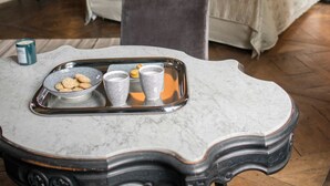 Un dormitorio moderno con una cama grande, un escritorio con silla, y una mesita de mármol con una bandeja de galletas y tazas.