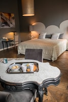Un dormitorio moderno con una cama grande, un escritorio con silla, y una mesita de mármol con una bandeja de galletas y tazas.