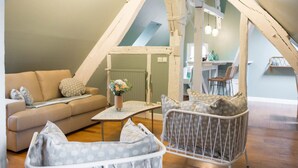 Un dormitorio tipo loft acogedor, con techo alto, un sofá, una silla y una mesita con un jarrón de flores.