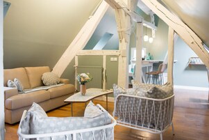 Un dormitorio tipo loft acogedor, con techo alto, un sofá, una silla y una mesita con un jarrón de flores.