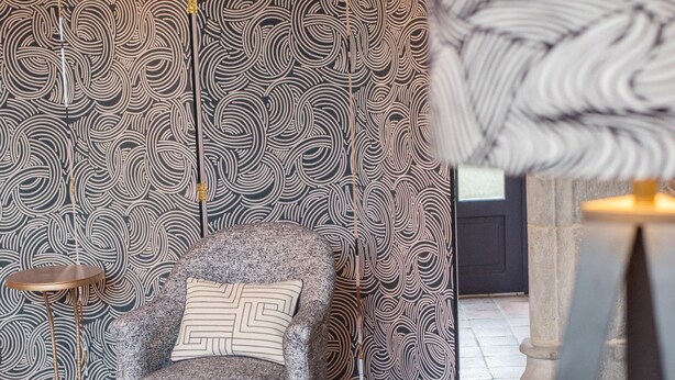Una habitación con pared decorada, un sillón gris con cojín estampado, una mesita redonda y una alfombra con diseño.