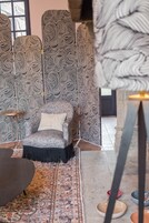 Una habitación con pared decorada, un sillón gris con cojín estampado, una mesita redonda y una alfombra con diseño.