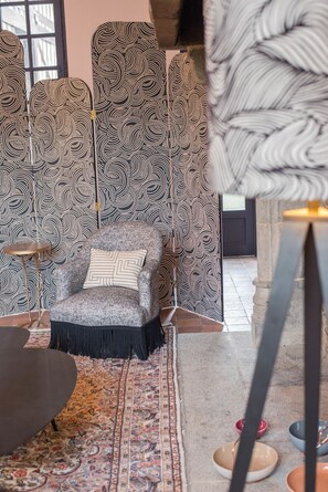Una habitación con pared decorada, un sillón gris con cojín estampado, una mesita redonda y una alfombra con diseño.