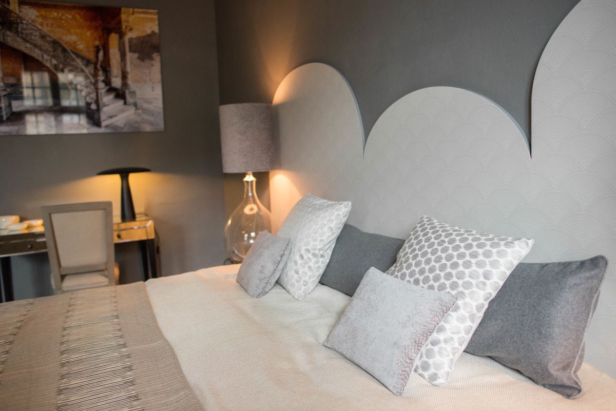 Un lit bien fait, avec une couvre-lit à motifs et plusieurs oreillers, une lampe sur une table de chevet et un tableau encadré au mur.