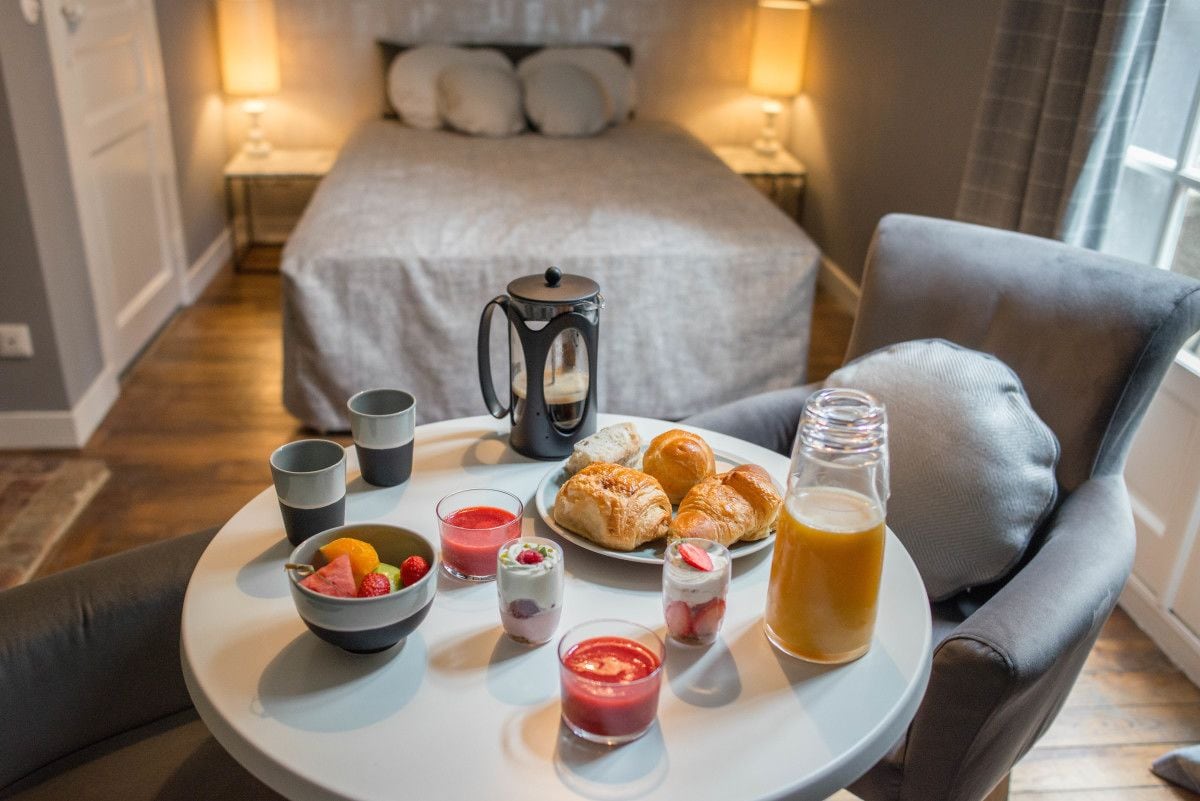 Bandeja de desayuno con croissants, fruta y bebidas sobre una mesa redonda en una habitación de hotel.