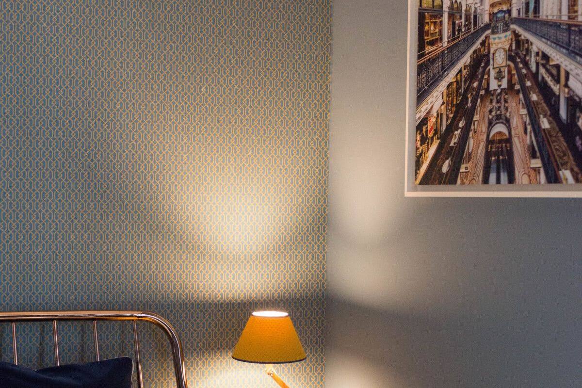 A neatly made bed with a metal frame, a bedside lamp, and a framed picture on the wall.