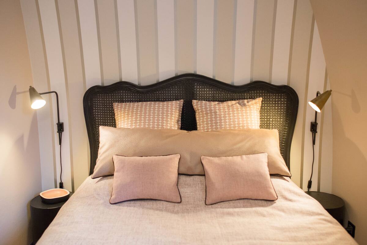 A neatly made bed with a headboard, two bedside lamps, and a small table with a bowl.