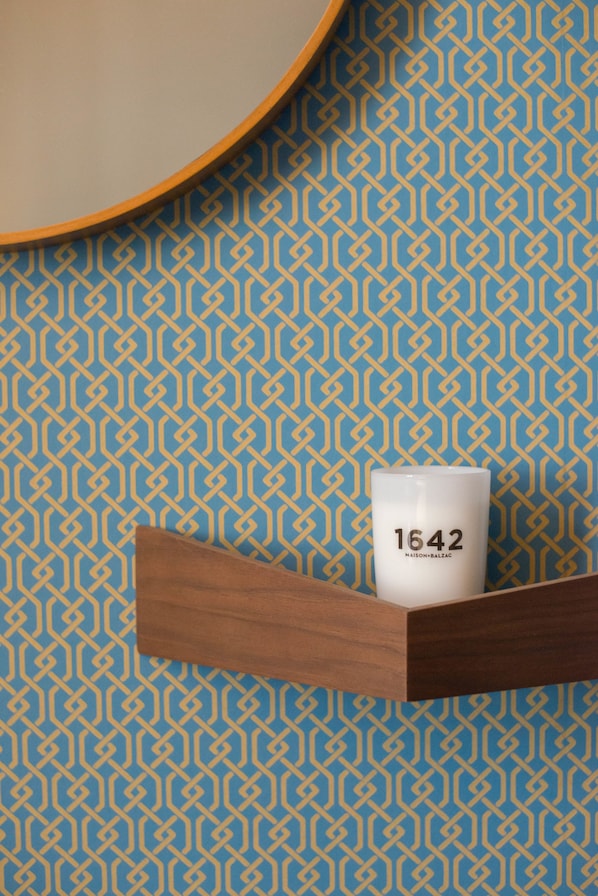 Una taza blanca con el número '1642', sobre un estante de madera frente a una pared azul con diseño.