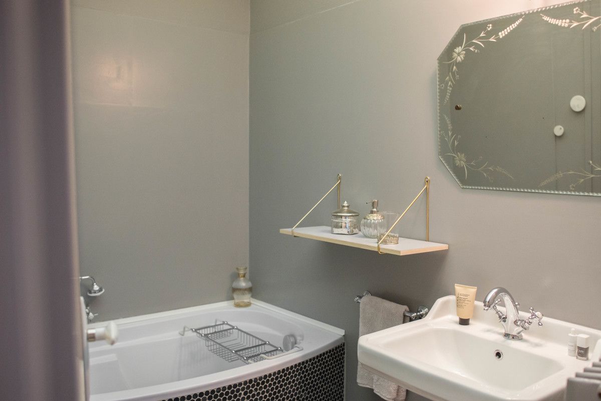 Een badkamer met een bad, een wastafel en een spiegel met een decoratief frame. Er zijn planken met toiletartikelen en een handdoekhouder.
