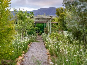 Un sendero en un jardín que lleva a un pérgola de madera, con vistas a montañas al fondo.