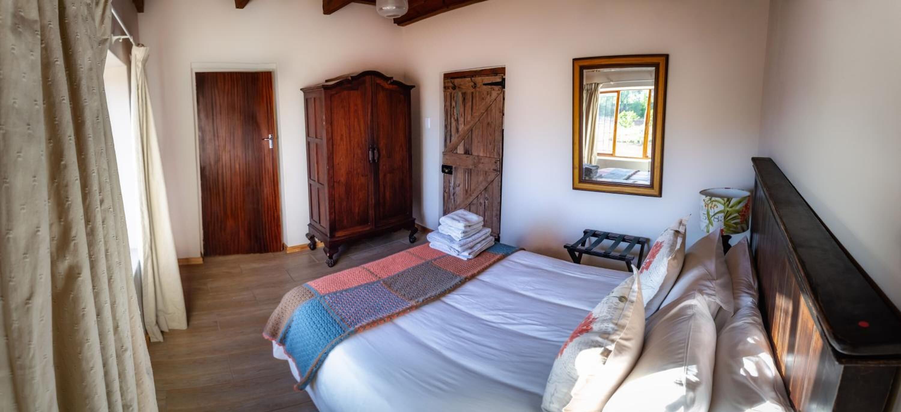 A bedroom with a large bed, wooden wardrobe, and a window with a view.