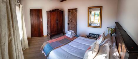 A bedroom with a large bed, wooden wardrobe, and a window with a view.