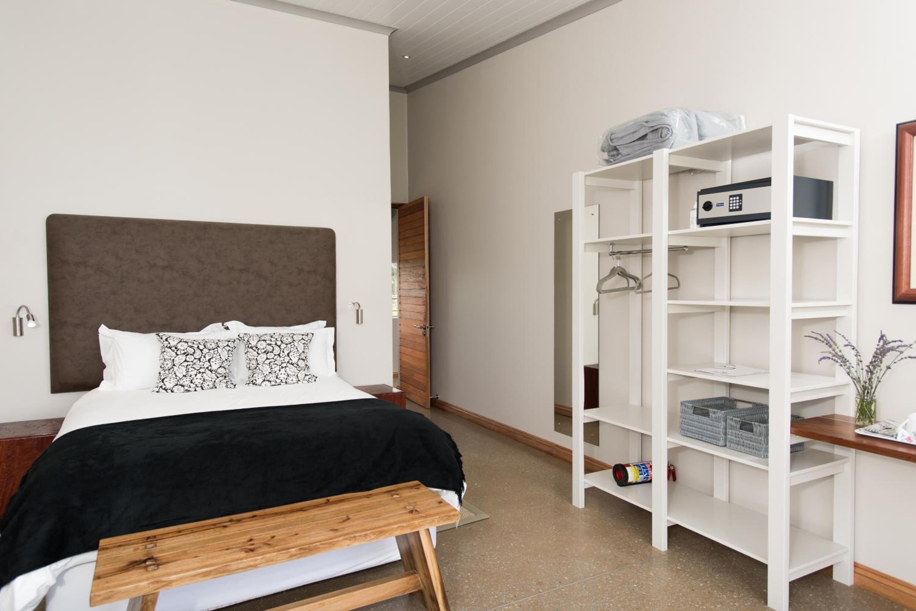 A modern bedroom with a bed, a wooden bench, a white wardrobe, and a small table with a vase.