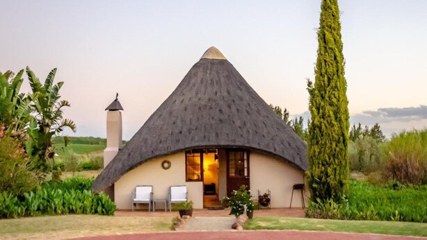 Une maison à toit de chaume avec une piscine devant.