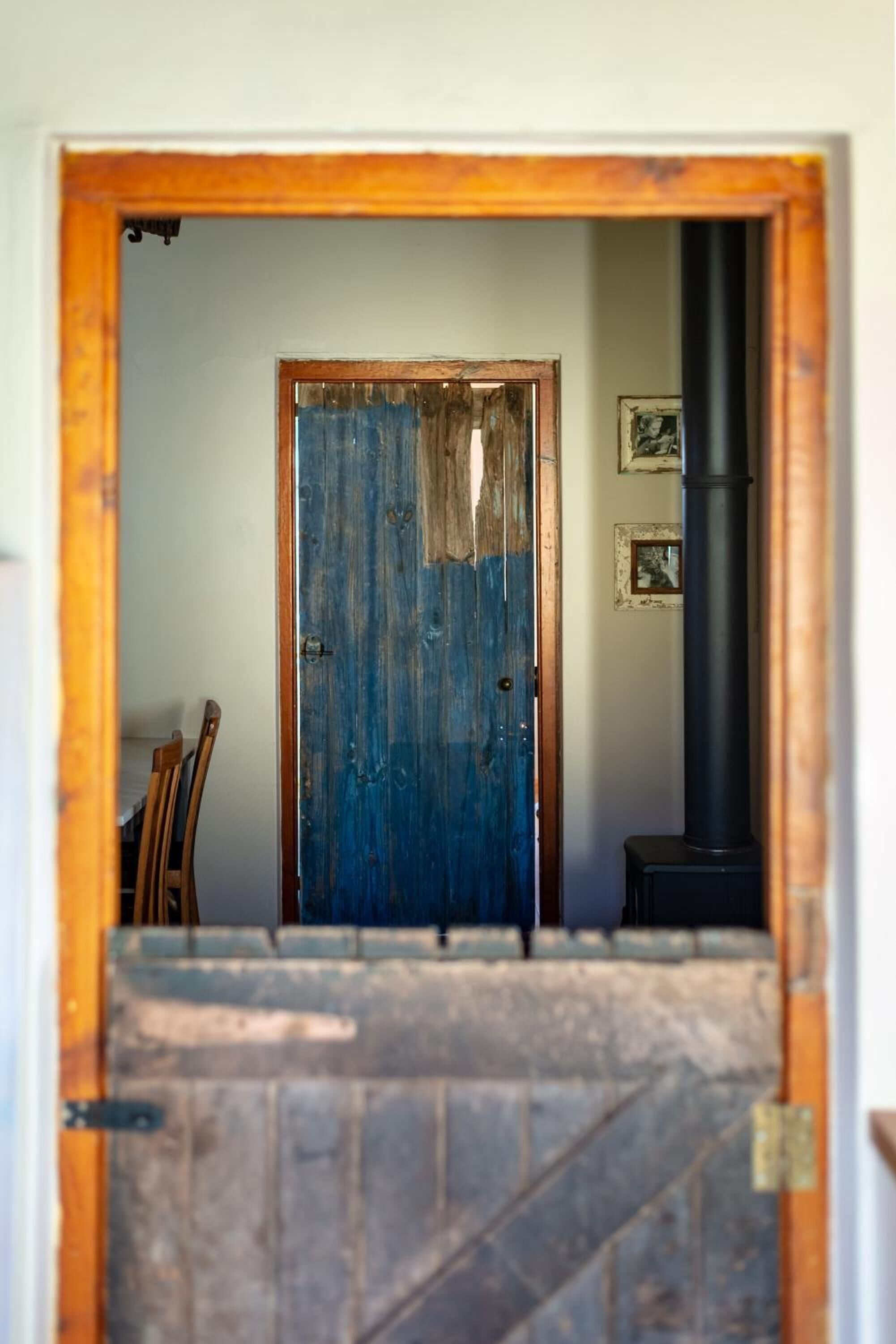A rustic wooden door with a blue paint finish, leading to a room with a black pipe and framed pictures on the wall.