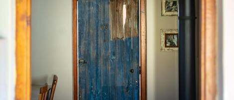 A rustic wooden door with a blue paint finish, leading to a room with a black pipe and framed pictures on the wall.