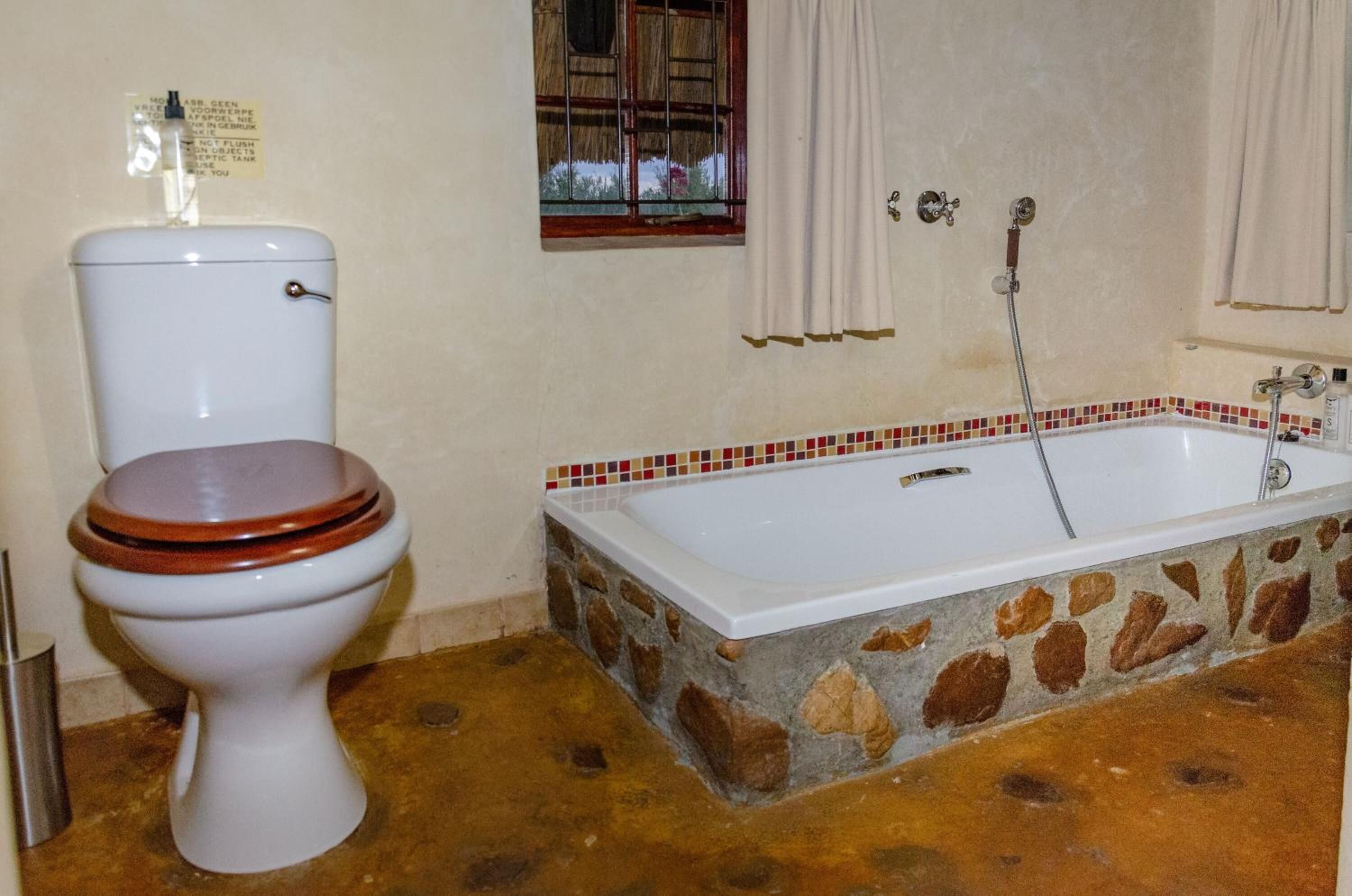 A bathroom with a toilet, a bathtub, and a window with curtains.