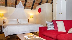 Une chambre d’hôtel avec un lit, un canapé rouge, une table en bois et un plafond recouvert d’un toit de chaume.