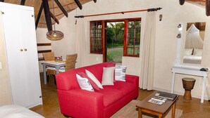 Un canapé rouge avec des coussins blancs, une table en bois, un meuble blanc et une batterie dans une pièce dotée d’un plafond haut et de poutres en bois.