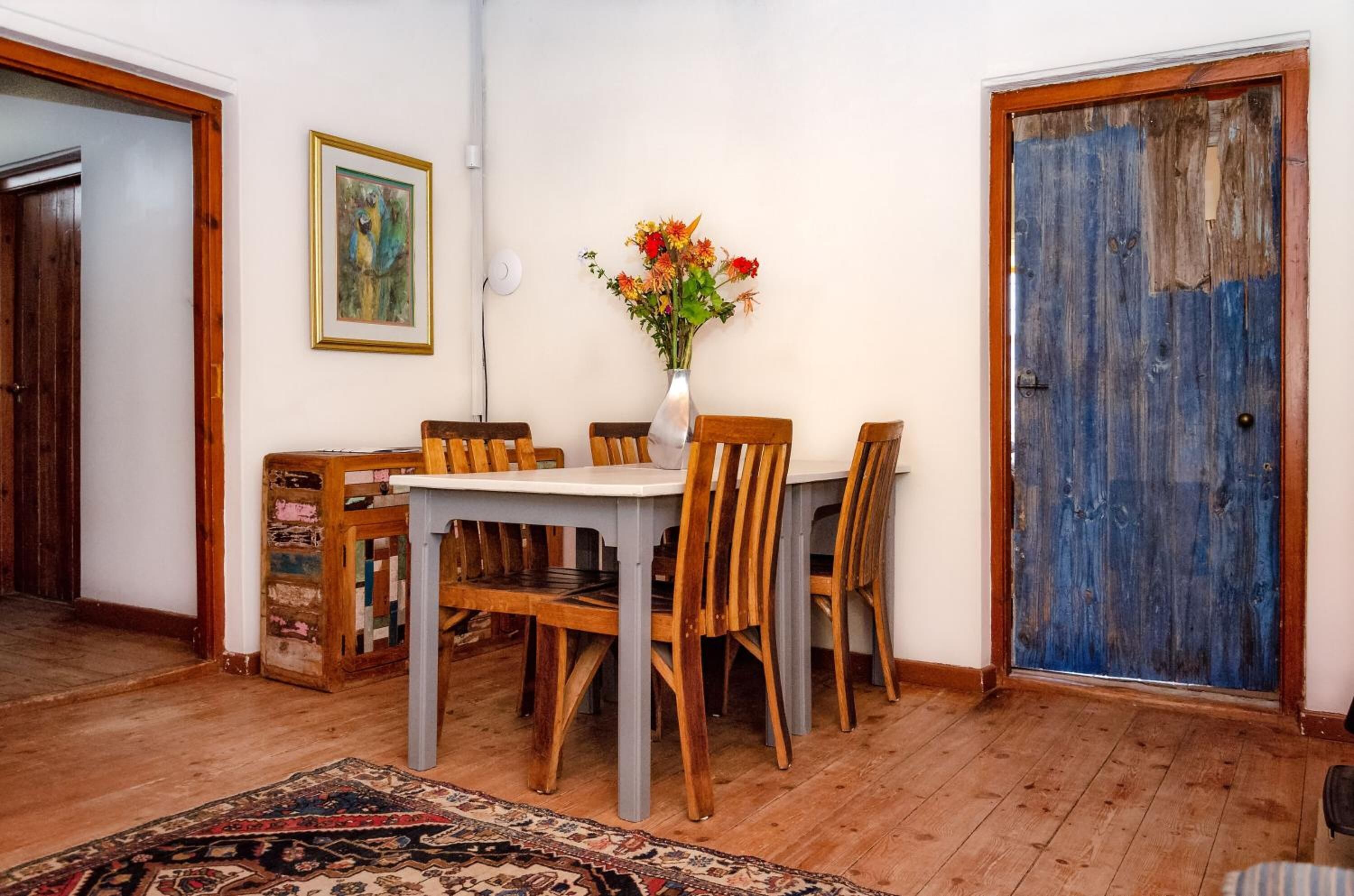 A dining area with a table and chairs, a vase with flowers, and a blue door.