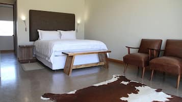A modern bedroom with a bed, two chairs, a wooden bedside table, a cowhide rug, and a nightstand.