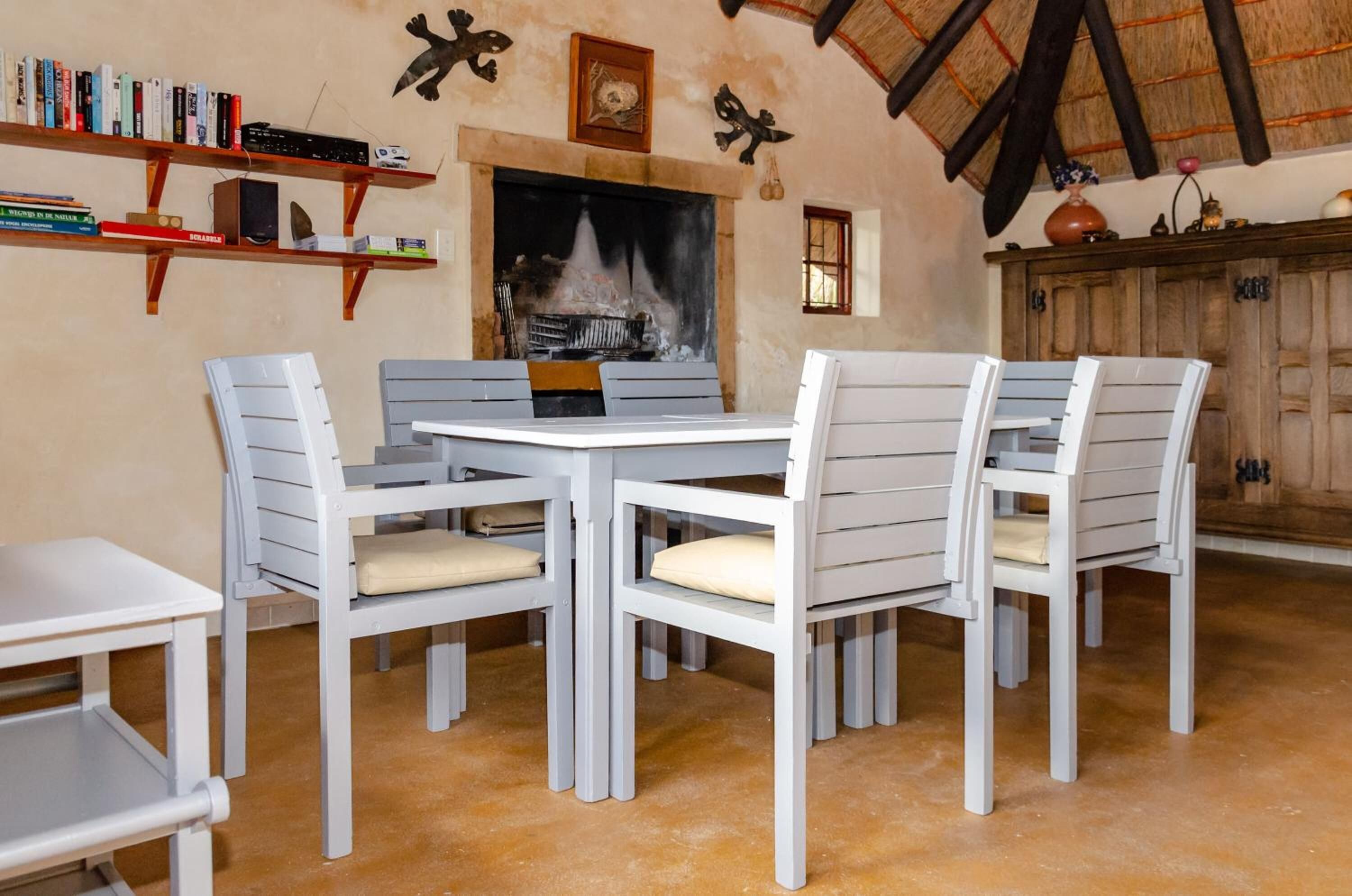 A dining area with a fireplace, white chairs, and a bookshelf.