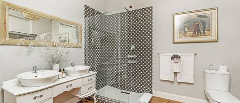 A bathroom with two sinks, a mirror, a shower, and a toilet.
