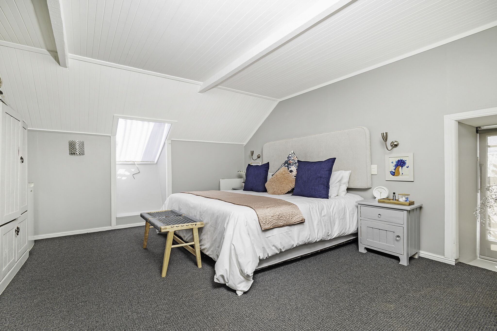 Ein Schlafzimmer mit einem Bett, Nachttischen, einer Bank, einem Fenster und einer Tür.