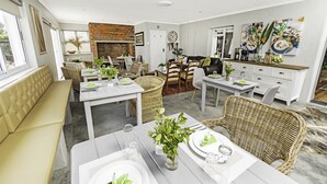 A spacious living area with a fireplace, dining tables set for meals, comfortable seating, and a kitchen area.