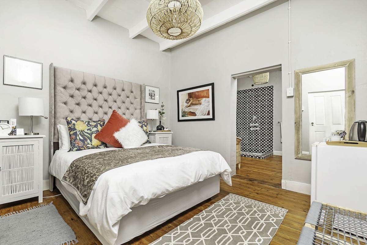 Une chambre à coucher avec une tête de lit capitonnée, un lit avec une literie à motifs, une table de chevet avec une lampe et un tapis à motifs géométriques.