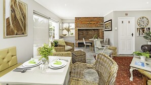 A modern living room with wicker furniture, a brick fireplace, and a dining area set for a meal.