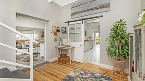 A spacious living area with a staircase, a large painting, a potted plant, and a view into the dining area.