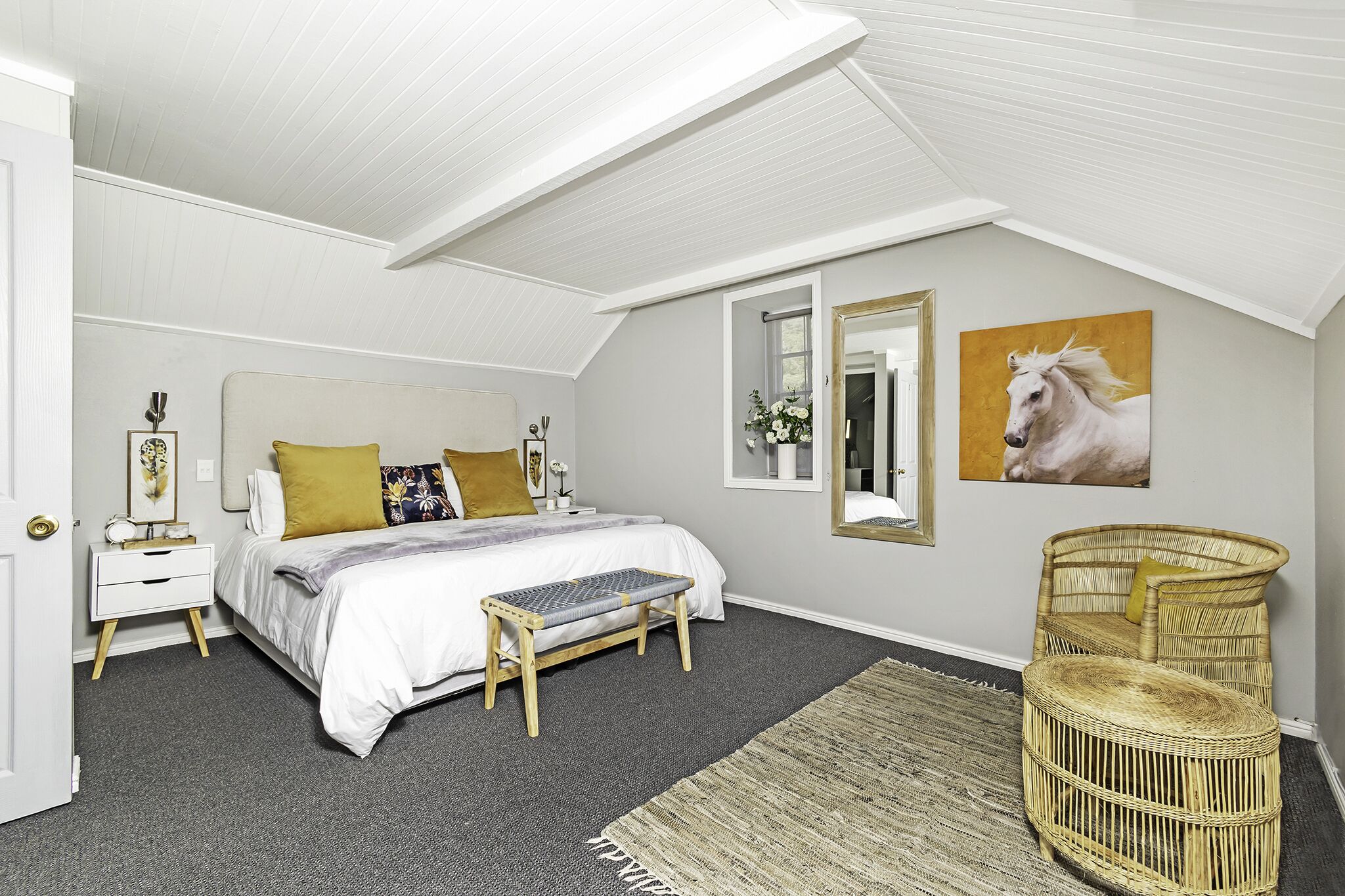 A bedroom with a bed, bedside table, bench, chair, and artwork.