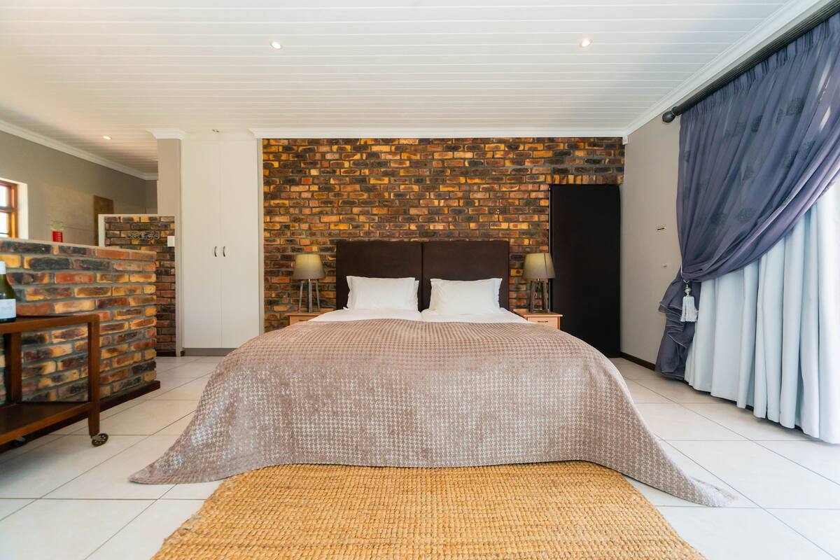 A bedroom with a brick-patterned headboard, a large bed with a patterned bedspread, two bedside lamps, and a view of a bathroom through an open door.